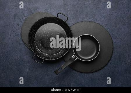 Kitchen cookware set with large paella pan and small frying pan on dark slate background, top view, both pans are black and rest on dark slate round p Stock Photo