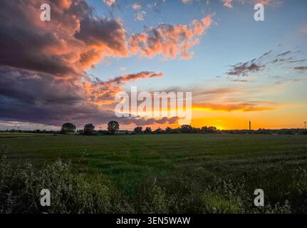 Wide rural landscape with open fields under a dramatic sunset sky. Colorful clouds are illuminated by the setting sun Stock Photo
