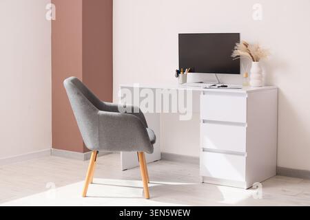 Modern home office workspace with computer monitor, white desk, and gray armchair in minimalist interior Stock Photo