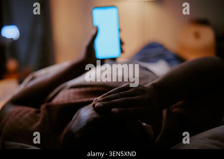 Black Man Lying in Bed Holding Smartphone for Sleep Disruption Stock Photo