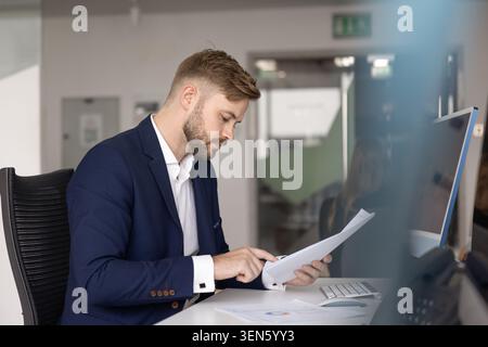 Businessman deeply focused on reading and analyzing printed financial reports Stock Photo
