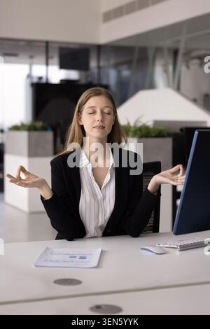 Young woman practicing meditation seated at workplace desk Stock Photo