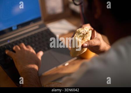 Adult Freelancer Eating While Using Laptop at Home Stock Photo
