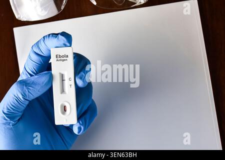 Gloved hand holding a negative Ebola antigen rapid test kit cassette in a medical laboratory or clinic setting, with copy space Stock Photo