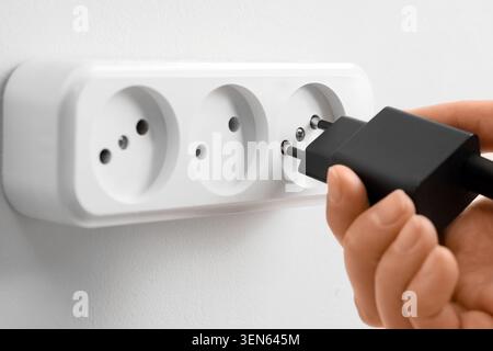 Hand plugging black charger into white wall power strip, electrical connection and energy supply Stock Photo