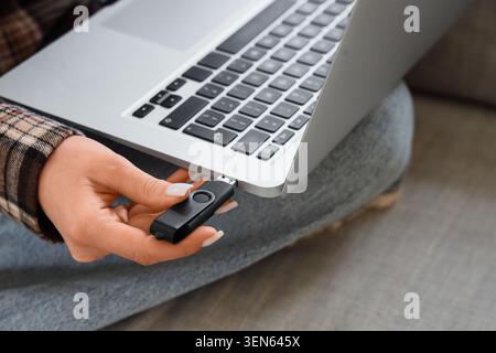 Female hand inserting USB flash drive into laptop port for data transfer and digital storage Stock Photo