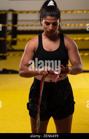 Female Boxer Putting On Hand Wraps in Boxing Ring Preparing For Training Session With Focused Determination Stock Photo