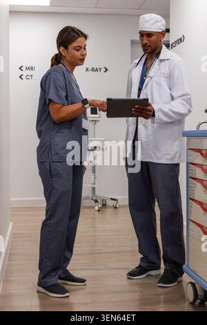 African American medical colleagues in scrubs and lab coat reviewing tablet in hospital corridor Stock Photo