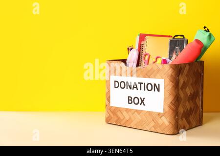 School supplies donation box with notebooks, pencils, and scissors for charity on yellow background Stock Photo