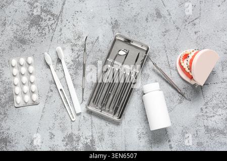 Dental health and orthodontic care tools with toothbrushes, pills, and jaw model on gray background Stock Photo
