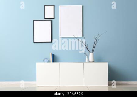 Modern home interior design with white cabinet, blank picture frames, and decorative vases on blue wall Stock Photo