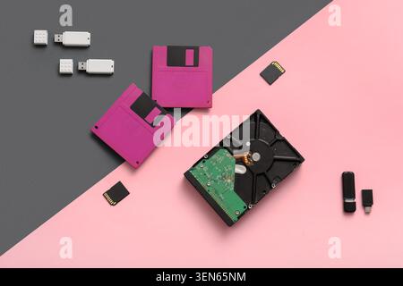 Digital data storage evolution: floppy disks, hard drive, USB flash drives, and memory cards on pink and gray background Stock Photo