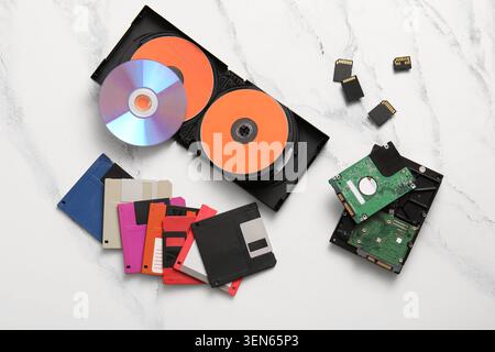 Evolution of data storage devices: floppy disks, cds, hard drives, and SD cards on white marble Stock Photo