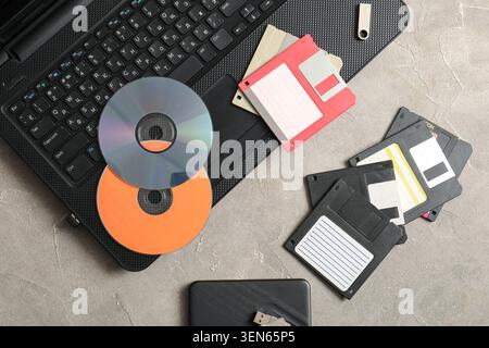 Digital data storage evolution: laptop, USB drive, cds, and floppy disks on concrete background Stock Photo