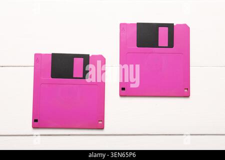 Two pink floppy disks on white wooden background, retro data storage technology and digital archiving, the magnetic media devices evoke nostalgia for Stock Photo