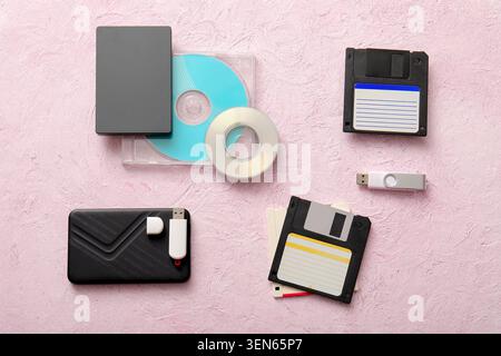 Evolution of data storage devices: floppy disks, cds, external hard drives, and USB flash drives on pink background Stock Photo