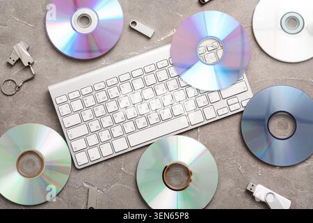 Digital data storage and computer peripherals flat lay with keyboard, cds, and USB drives on gray background Stock Photo