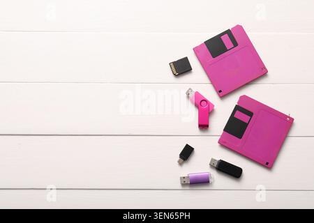 Retro pink floppy disks, USB flash drives, and SD card on white wooden background, data storage evolution Stock Photo