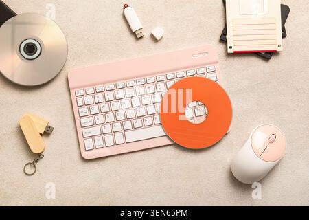 Retro and modern computer peripherals with pink keyboard, mouse, floppy disks, cds, and USB drives on textured background Stock Photo