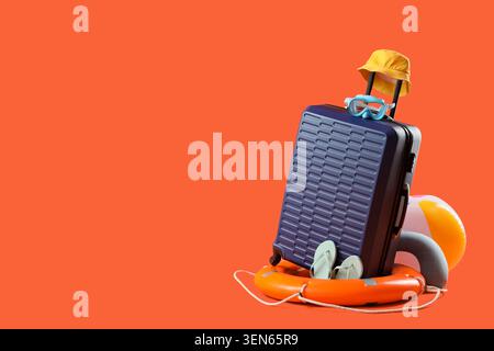Summer vacation travel with blue suitcase yellow hat goggles flip-flops lifebuoy and beach ball on orange background, the travel items are arranged on Stock Photo