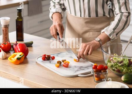 Woman chopping fresh cherry tomatoes on marble cutting board for healthy salad preparation in modern kitchen, various vegetables and cooking ingredien Stock Photo