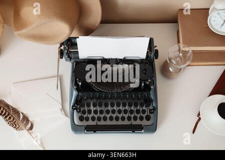 Vintage typewriter with blank paper, feather pen, envelopes, and coffee on white desk for creative writing Stock Photo