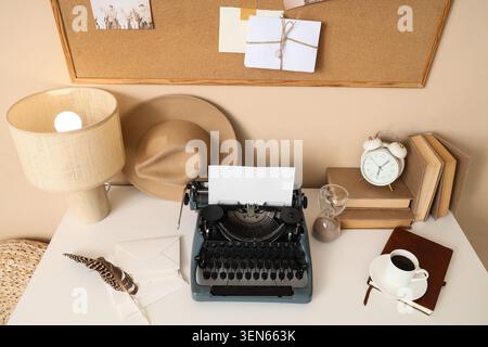 Vintage typewriter with blank paper on creative writer's desk, cork board, books, coffee, and feather pen Stock Photo