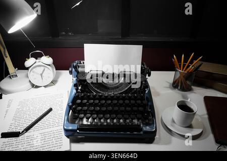Vintage typewriter with blank paper, desk lamp, alarm clock, and coffee cup on a white table for creative writing Stock Photo