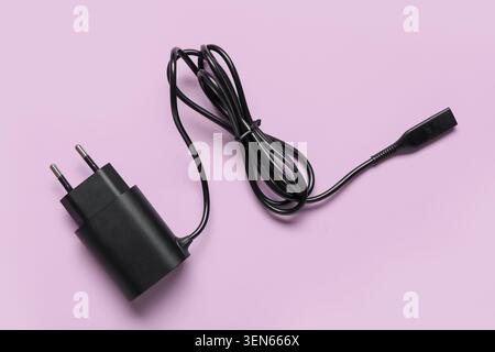 Black USB power adapter and charging cable for electronic devices on a light purple background, the adapter features two metal prongs for electrical o Stock Photo