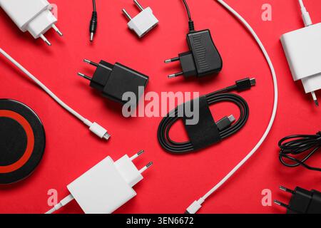 Assorted electronic device chargers and cables for modern technology on red background Stock Photo