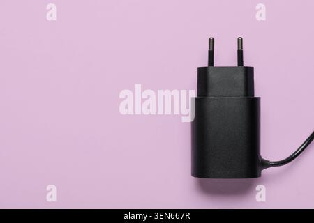 Black USB wall charger adapter with two prongs and cable on a light purple background Stock Photo