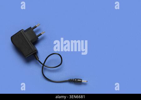 Black AC power adapter with DC connector and cable on blue background, electronic device charging technology, this electronic device is used for charg Stock Photo