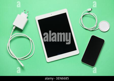 Modern digital tablet, smartphone, charger, and wireless charging pad on green background for technology and connectivity Stock Photo