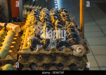 A high-angle, close-up shot of black century eggs, each individually wrapped in clear plastic packaging and arranged in cardboard egg cartons. Stock Photo