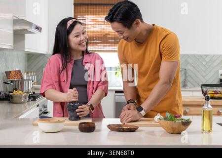 Asian couple cooking at white countertop, crushing with mortar and pestle, chopping on wooden board Stock Photo