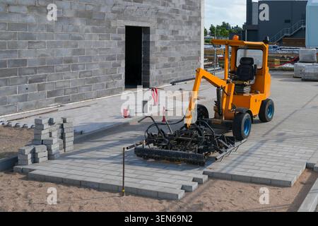 Mechanical paving machine laying concrete paving blocks around a new industrial building during site development works Stock Photo