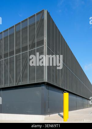 Low-angle view of a contemporary logistics warehouse corner featuring metal mesh cladding and safety bollard Stock Photo