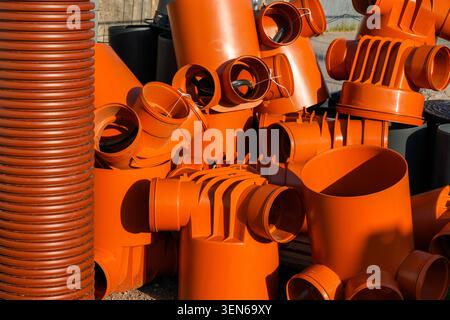 Orange PVC sewer and drainage pipe fittings stacked outdoors for underground utility, stormwater and sewer installation projects Stock Photo