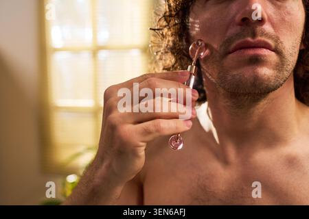 Adult Man Using Facial Roller during Skincare Routine at Home Stock Photo