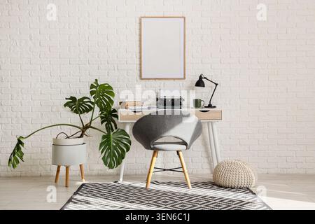 Modern home office workspace with monstera plant, typewriter, and blank frame on white brick wall Stock Photo