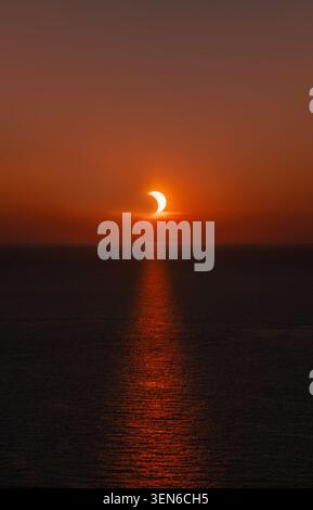 Partial solar eclipse at sunset over the ocean with the sun's reflection on the water of the Mediterranean near Menorca Stock Photo
