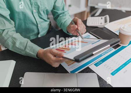 Business professional analyzing financial reports, reviewing performance charts and calculating budget figures using digital devices, supporting data- Stock Photo