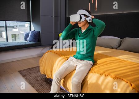 White VR headset with headphones is resting on edge of mustard bed near window seat Stock Photo