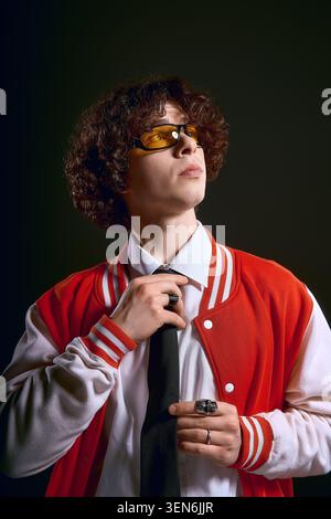 Handsome young man wearing fashionable glasses and a varsity jacket expresses deep emotions. Stock Photo