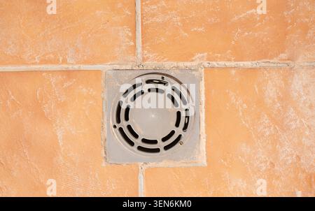 Close up top view of a circular gray plastic drain cover installed in the middle of outdoor terracotta ceramic floor tiles. Stock Photo