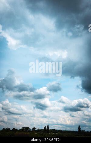 Dramatic cloudy sky over a green landscape, with dark storm clouds and soft blue light after rain Stock Photo