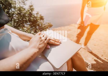 Jewelry laptop rings on womans hands resting on a silver computer while sitting outdoors on a bright and sunny summer day Stock Photo