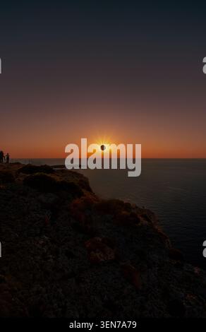 Silhouettes of people and a family with the father lifting his son to observe a total solar eclipse with a prominent starburst over the ocean coast of Stock Photo
