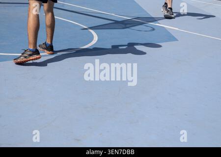 Players' legs and shadows moving on a light blue outdoor basketball court Stock Photo