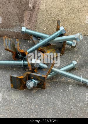 Close-up of steel bolts and rusty brackets on asphalt - industrial construction hardware, engineering, repair and maintenance concept. Stock Photo